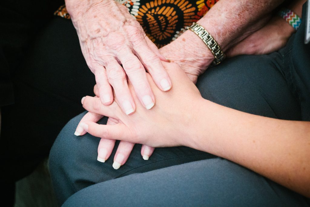 A resident holds hands with a nurse at a memory care facility