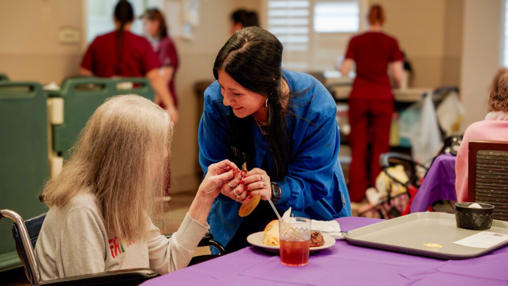 A nurse assists a long term care resident at a dinner table