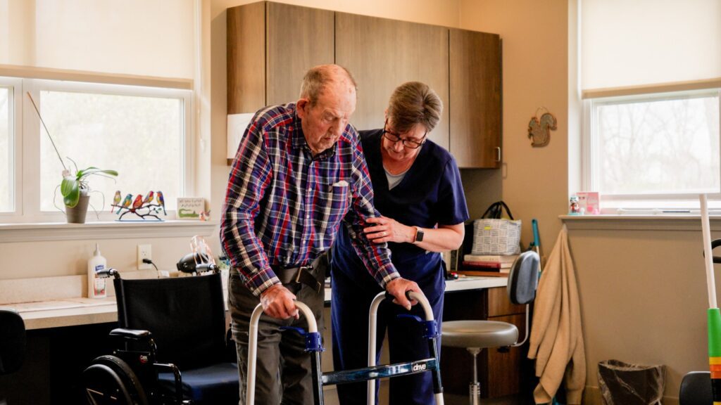 A man walks with the assistance of a nurse at a skilled nursing facility, offering long-term care